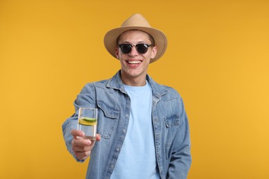 Photo of Happy man in sunglasses and hat with glass of refreshing drink on yellow background