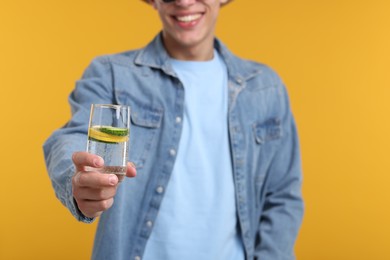 Photo of Happy man with glass of refreshing drink on yellow background, closeup