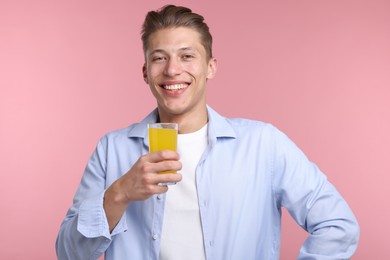 Photo of Happy man with glass of orange juice on pink background. Refreshing drink