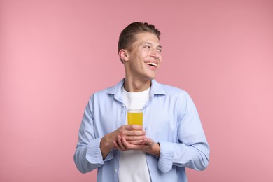 Photo of Happy man with glass of orange juice on pink background. Refreshing drink