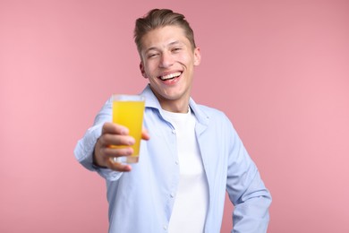 Photo of Happy man with glass of orange juice on pink background. Refreshing drink