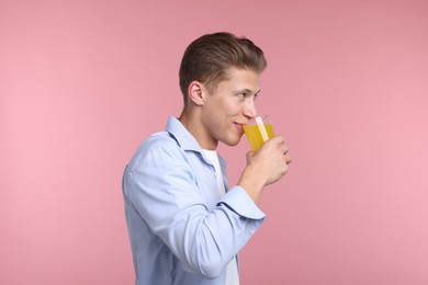 Photo of Man drinking orange juice from glass on pink background. Refreshing drink