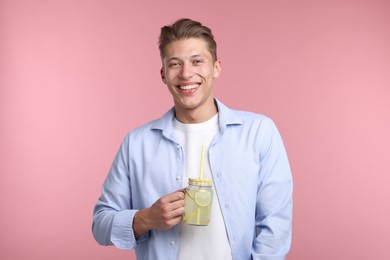 Photo of Happy man with mason jar of lemonade on pink background. Refreshing drink
