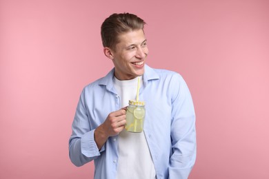 Photo of Happy man with mason jar of lemonade on pink background. Refreshing drink