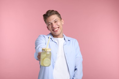 Photo of Happy man with mason jar of lemonade on pink background. Refreshing drink