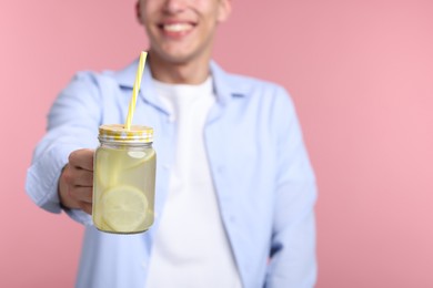 Photo of Happy man with mason jar of lemonade on pink background, closeup. Refreshing drink