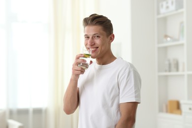 Photo of Happy man drinking healthy beverage from glass at home. Refreshing drink