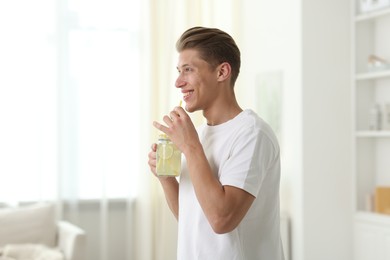 Photo of Happy man with mason jar of lemonade at home. Refreshing drink
