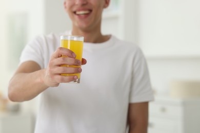 Photo of Smiling man with glass of orange juice at home, closeup. Refreshing drink