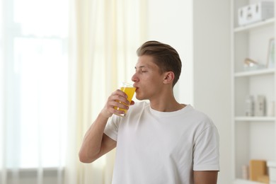 Photo of Man drinking orange juice from glass at home. Refreshing drink