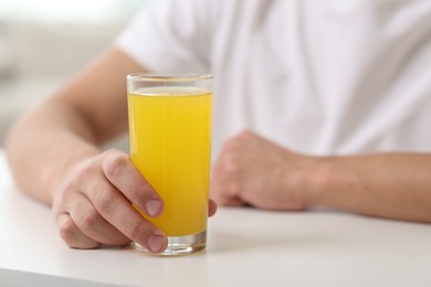 Photo of Man with glass of orange juice at white table indoors, closeup. Refreshing drink