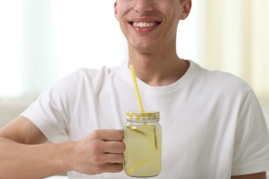 Photo of Happy man with mason jar of lemonade at home, closeup. Refreshing drink