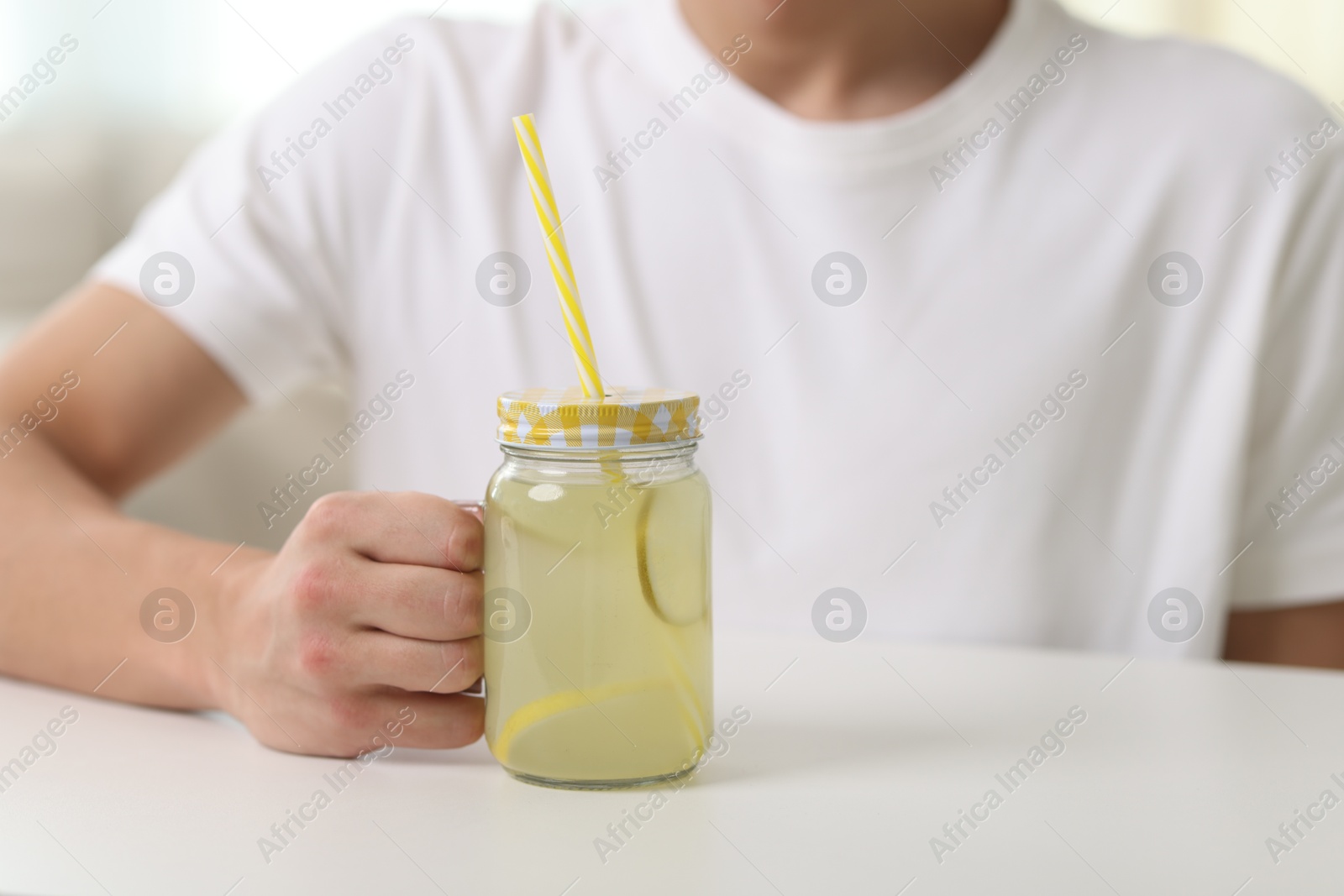 Man with mason jar of lemonade at white table indoors, closeup. Refreshing drink Photo of Man with mason jar of lemonade at white table indoors, closeup. Refreshing drink