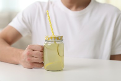 Photo of Man with mason jar of lemonade at white table indoors, closeup. Refreshing drink