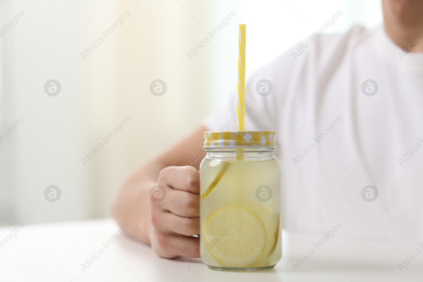 Photo of Man with mason jar of lemonade at white table indoors, closeup with space for text. Refreshing drink
