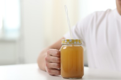 Photo of Man with mason jar of orange juice at white table indoors, closeup with space for text. Refreshing drink