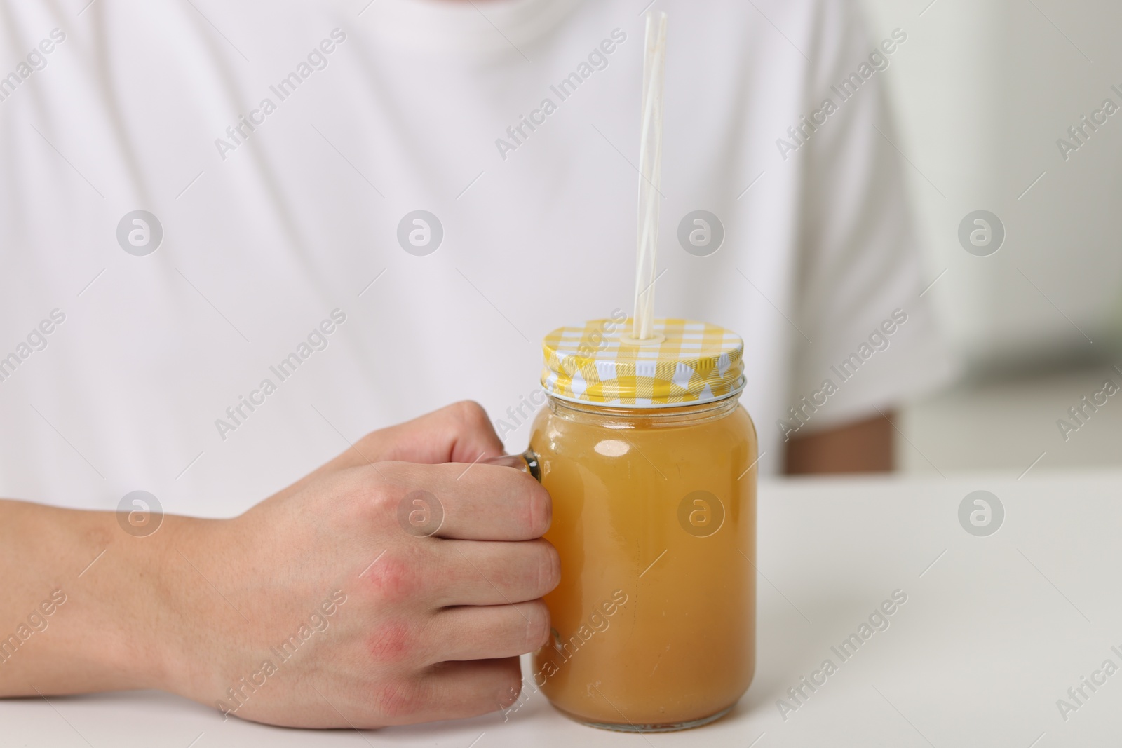 Man with mason jar of orange juice at white table indoors, closeup. Refreshing drink Photo of Man with mason jar of orange juice at white table indoors, closeup. Refreshing drink