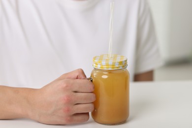 Photo of Man with mason jar of orange juice at white table indoors, closeup. Refreshing drink