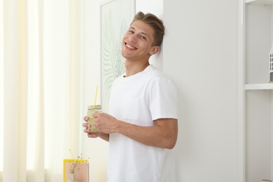 Photo of Happy man with mason jar of lemonade near white wall at home. Refreshing drink