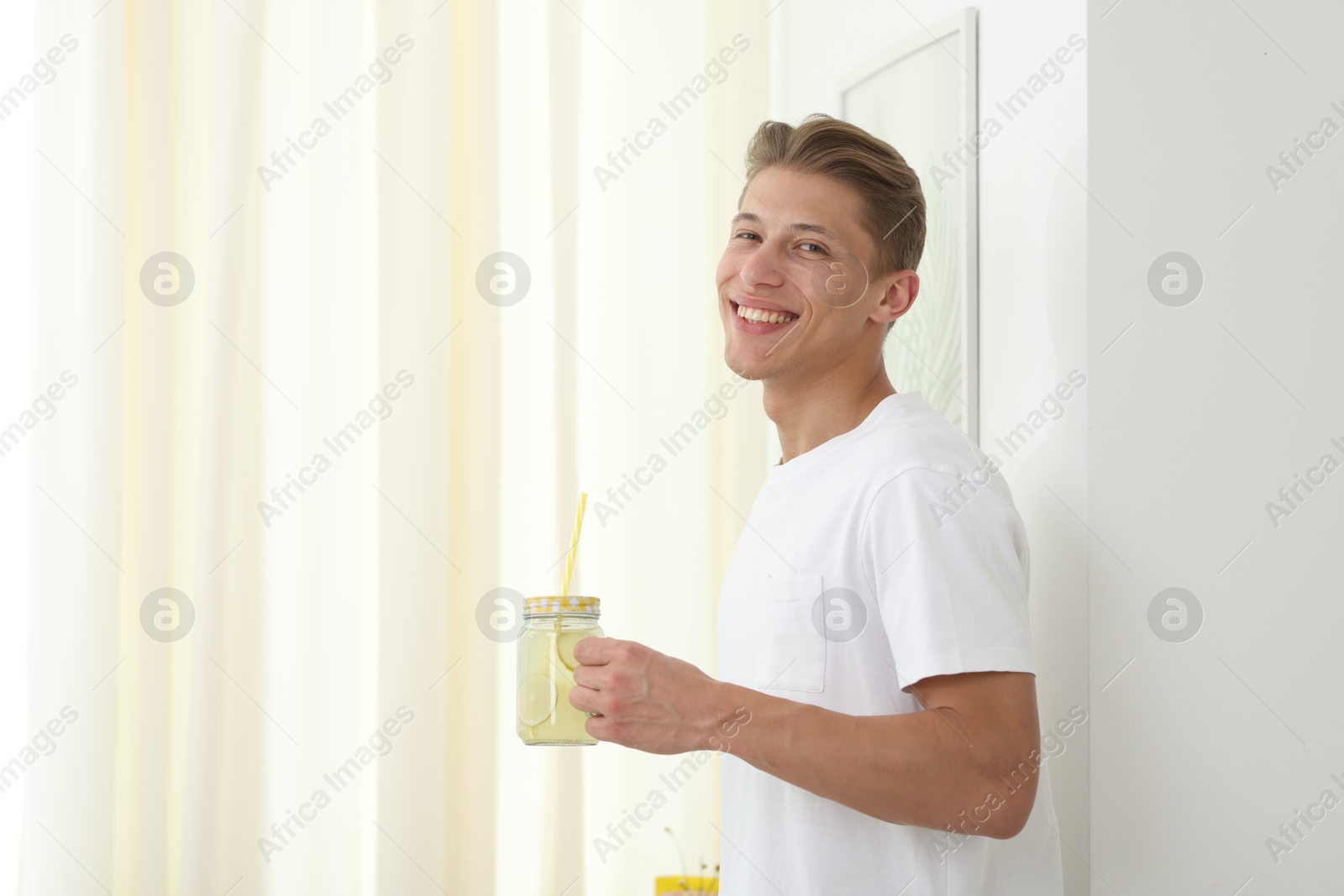 Happy man with mason jar of lemonade near white wall at home, space for text. Refreshing drink Photo of Happy man with mason jar of lemonade near white wall at home, space for text. Refreshing drink