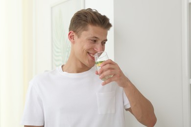 Photo of Smiling man drinking healthy beverage from glass at home. Refreshing drink