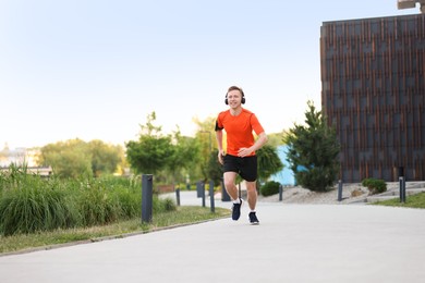Photo of Smiling sportsman in headphones with armband running outdoors, low angle view. Morning exercise