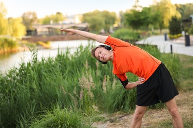 Photo of Young sportsman in headphones doing morning exercise outdoors