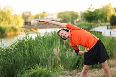 Photo of Smiling sportsman in headphones doing morning exercise outdoors