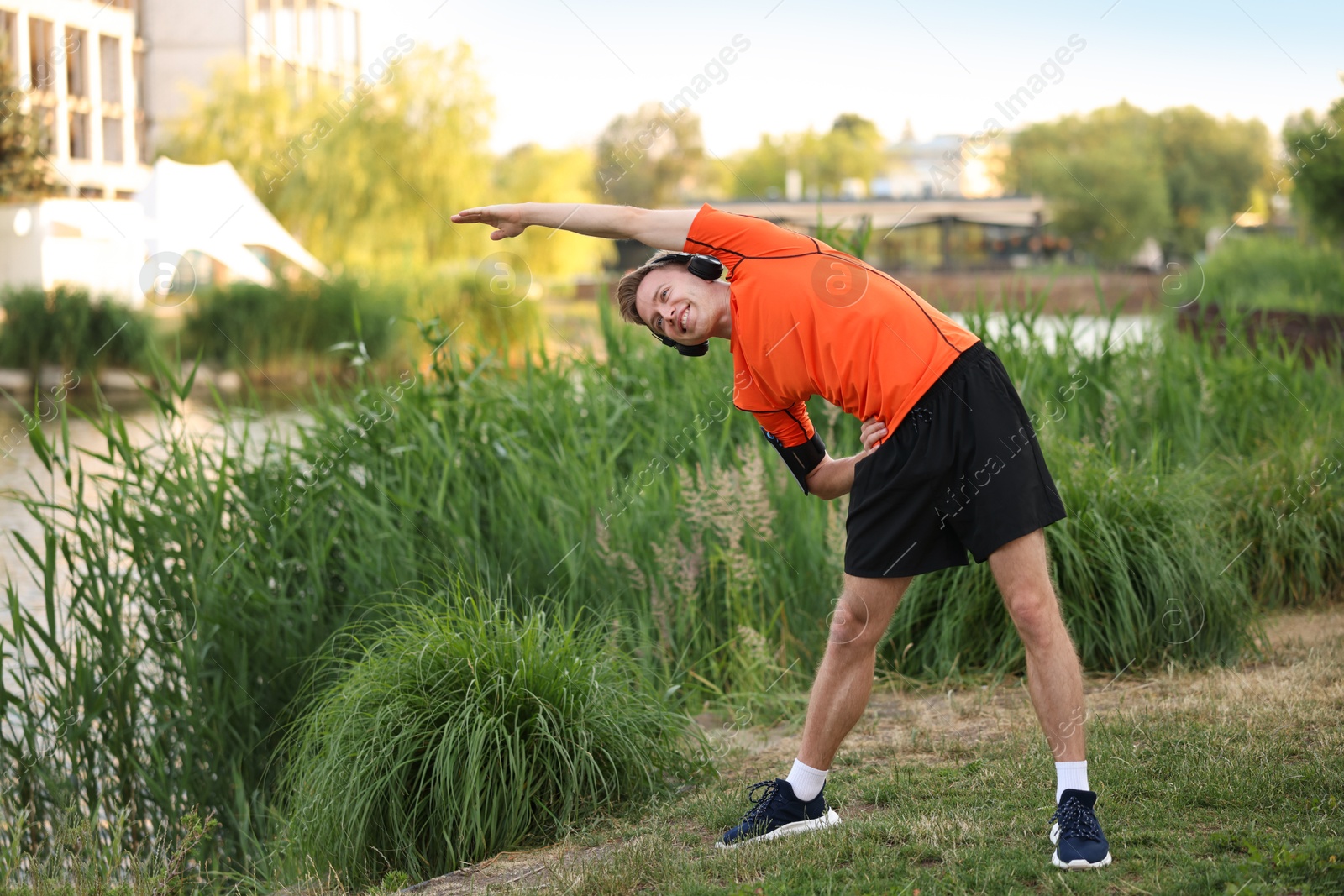 Photo of Smiling sportsman in headphones doing morning exercise outdoors