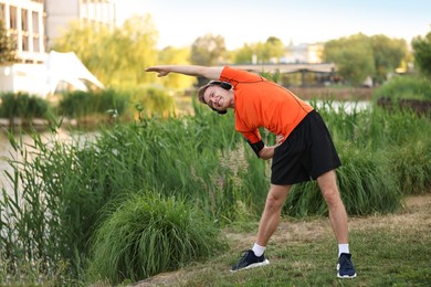 Photo of Smiling sportsman in headphones doing morning exercise outdoors