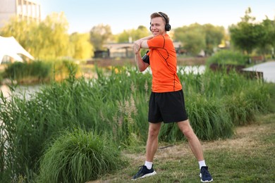 Photo of Smiling sportsman in headphones doing morning exercise outdoors