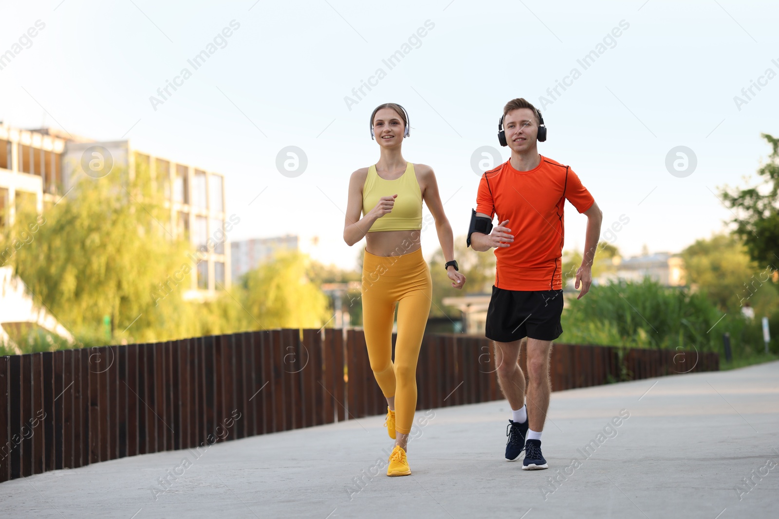 Photo of Happy couple in headphones running outdoors, low angle view. Morning exercise