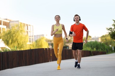 Photo of Happy couple in headphones running outdoors, low angle view. Morning exercise