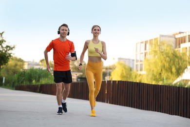 Photo of Happy couple in headphones running outdoors, low angle view. Morning exercise