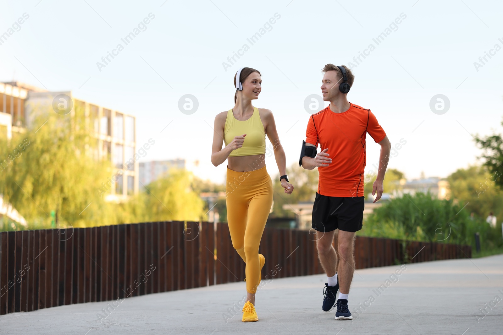 Photo of Happy couple in headphones running outdoors, low angle view. Morning exercise