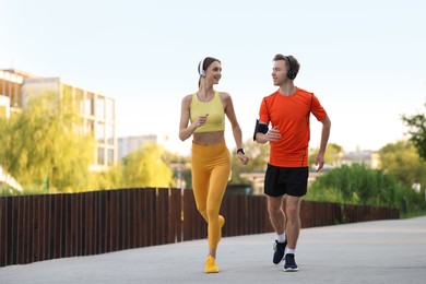 Photo of Happy couple in headphones running outdoors, low angle view. Morning exercise