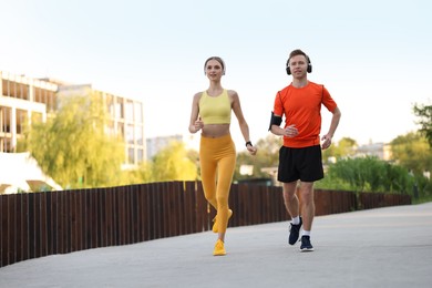 Photo of Happy couple in headphones running outdoors, low angle view. Morning exercise