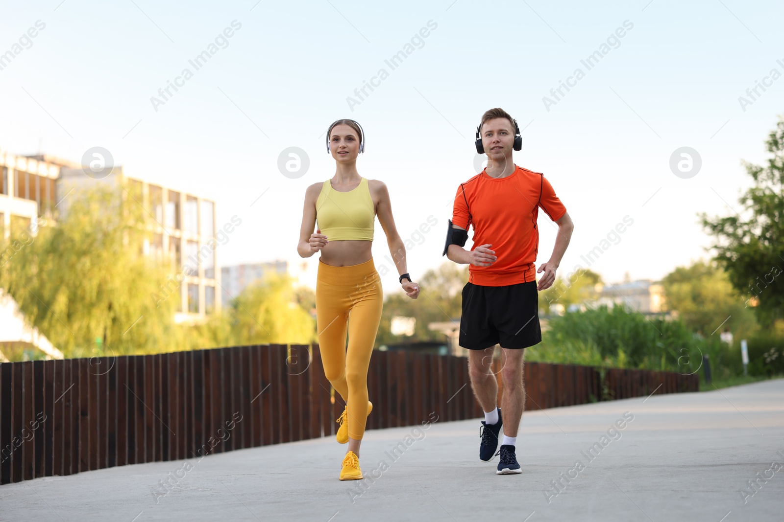 Photo of Happy couple in headphones running outdoors, low angle view. Morning exercise