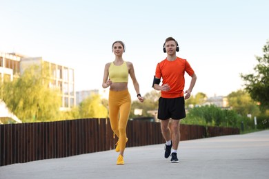 Photo of Happy couple in headphones running outdoors, low angle view. Morning exercise