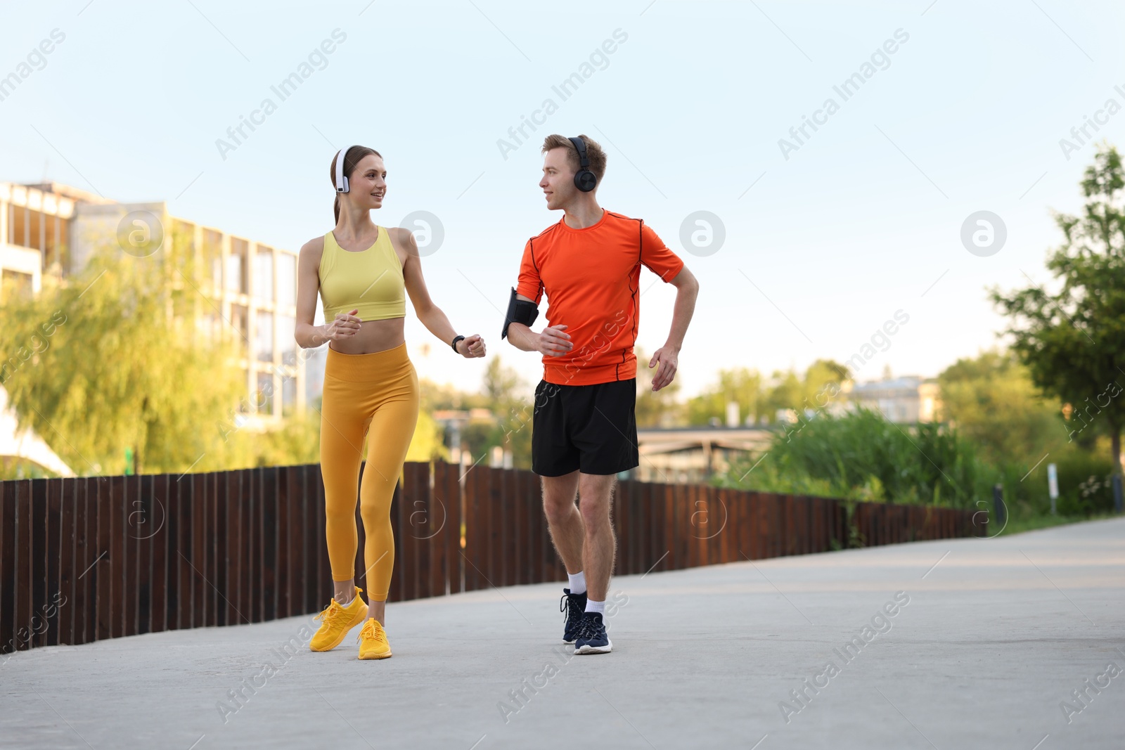 Photo of Happy couple in headphones running outdoors, low angle view. Morning exercise