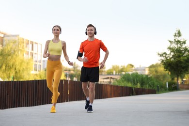 Photo of Happy couple in headphones running outdoors, low angle view. Morning exercise