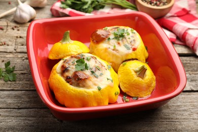 Photo of Tasty stuffed pattypan squashes in baking dish on wooden table, closeup