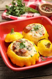 Photo of Tasty stuffed pattypan squashes in baking dish on wooden table, closeup