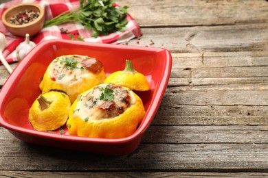 Photo of Tasty stuffed pattypan squashes in baking dish on wooden table, closeup. Space for text