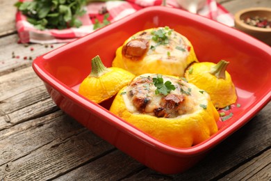 Photo of Tasty stuffed pattypan squashes in baking dish on wooden table, closeup