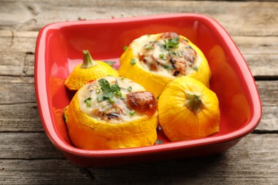 Photo of Tasty stuffed pattypan squashes in baking dish on wooden table, closeup