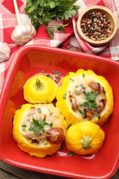 Photo of Tasty stuffed pattypan squashes in baking dish and spices on wooden table, flat lay
