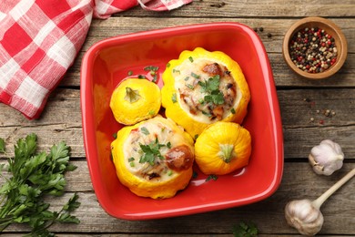 Photo of Tasty stuffed pattypan squashes in baking dish and spices on wooden table, flat lay