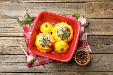 Photo of Tasty stuffed pattypan squashes in baking dish and spices on wooden table, flat lay