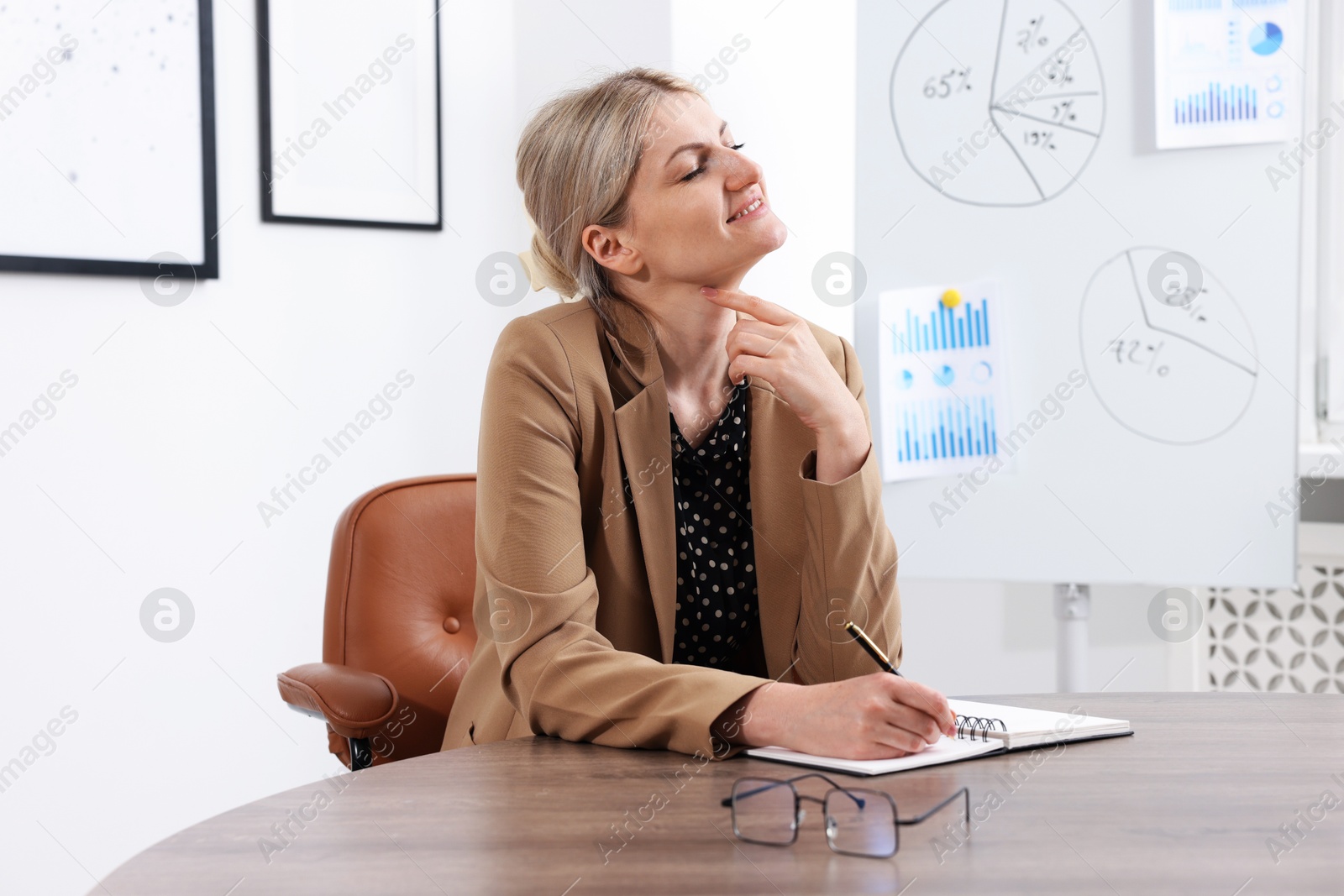 Dreams come true. Happy woman thinking about something while taking notes at wooden table indoors Photo of Dreams come true. Happy woman thinking about something while taking notes at wooden table indoors